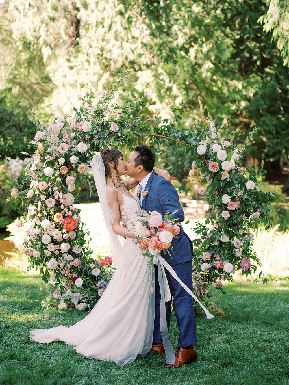 bride and groom kiss in front of floral arch