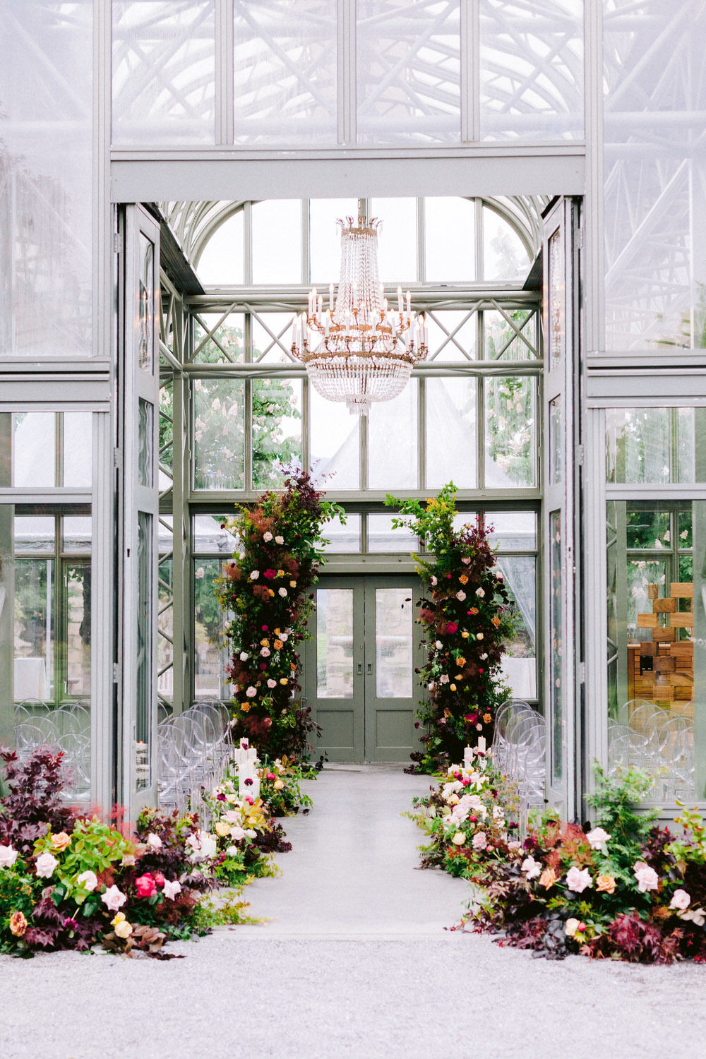 lush greenery, colorful florals, candles and ghost chairs decorate this greenhouse